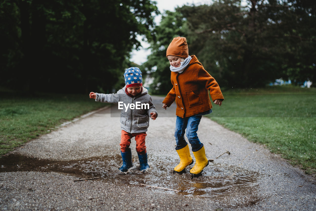 Two boys jumping in the puddles at the park on cloudy day