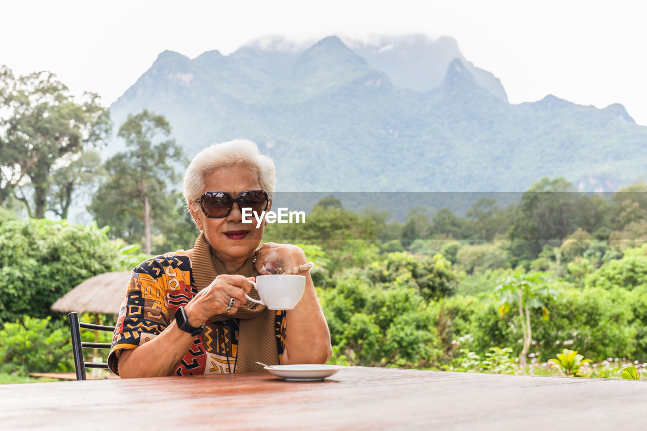 Asin grey white hair senior woman drinking coffee in cafe outdoor with mountain view