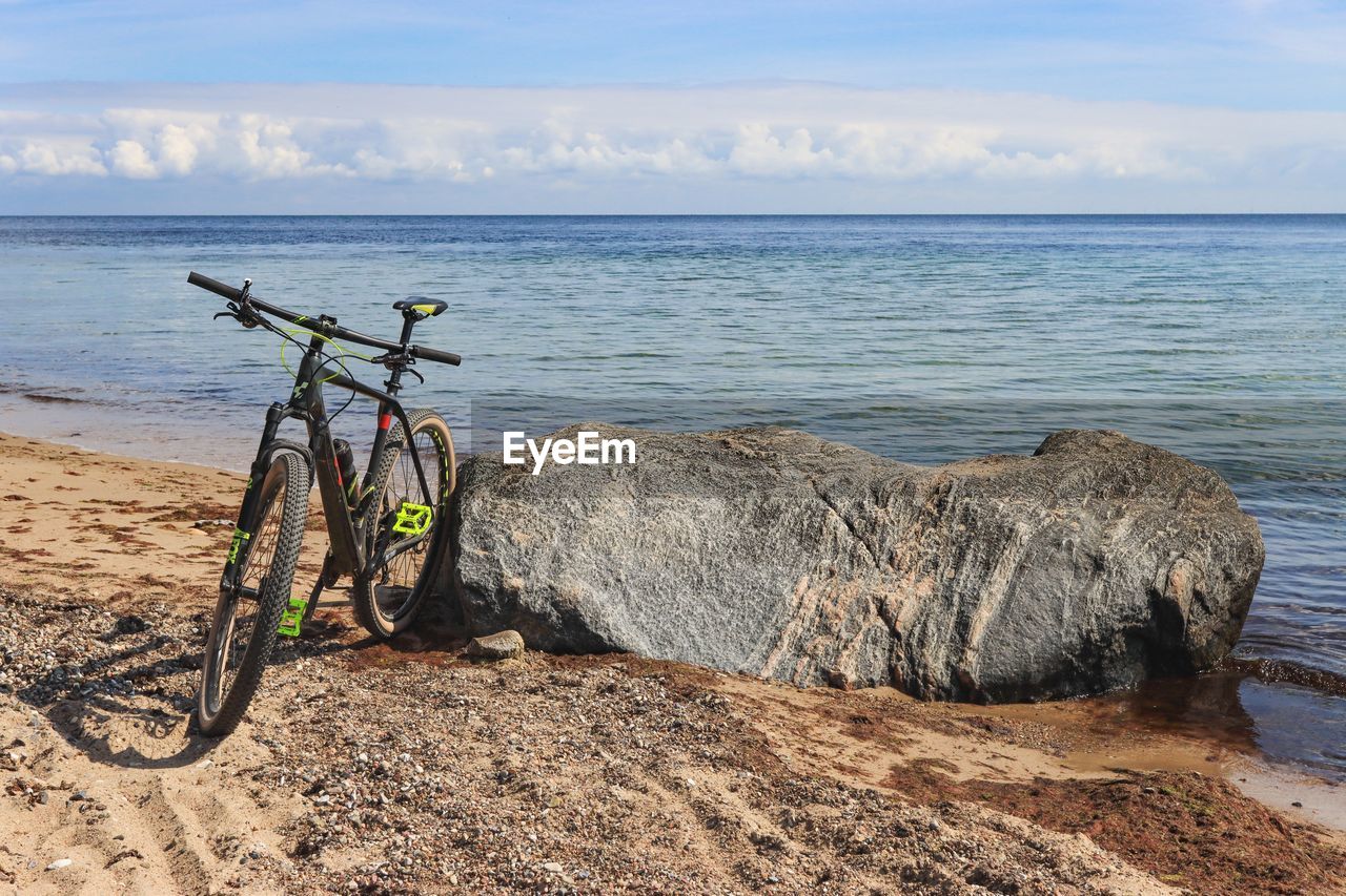 water, bicycle, sea, land, beach, sky, vehicle, nature, transportation, horizon over water, horizon, sand, beauty in nature, shore, scenics - nature, coast, tranquility, mode of transportation, day, tranquil scene, sports equipment, cloud, no people, bicycle wheel, outdoors, travel, sunlight, land vehicle, ocean, non-urban scene, rock, body of water, idyllic, tire
