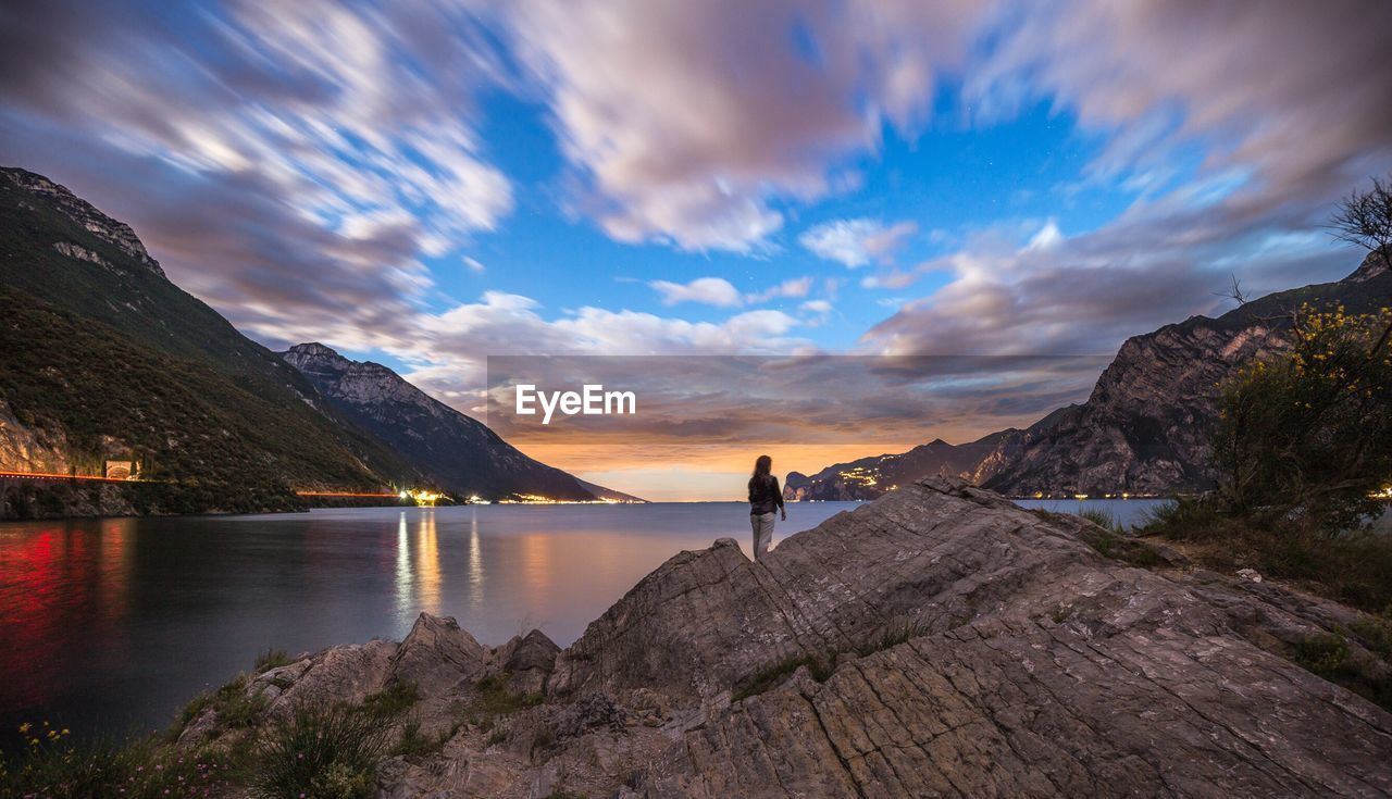 Woman standing on rock against lake during sunset