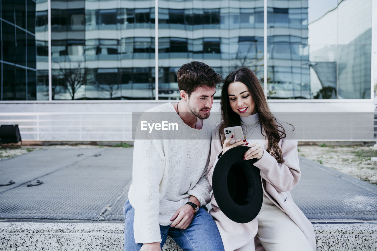 Smiling woman showing mobile phone to male partner in city