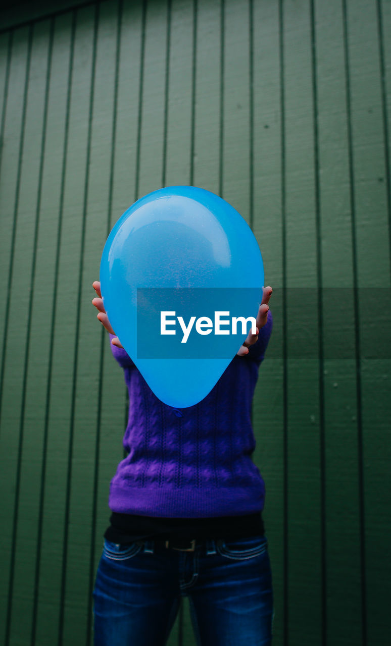 Woman holding blue balloon against wooden wall