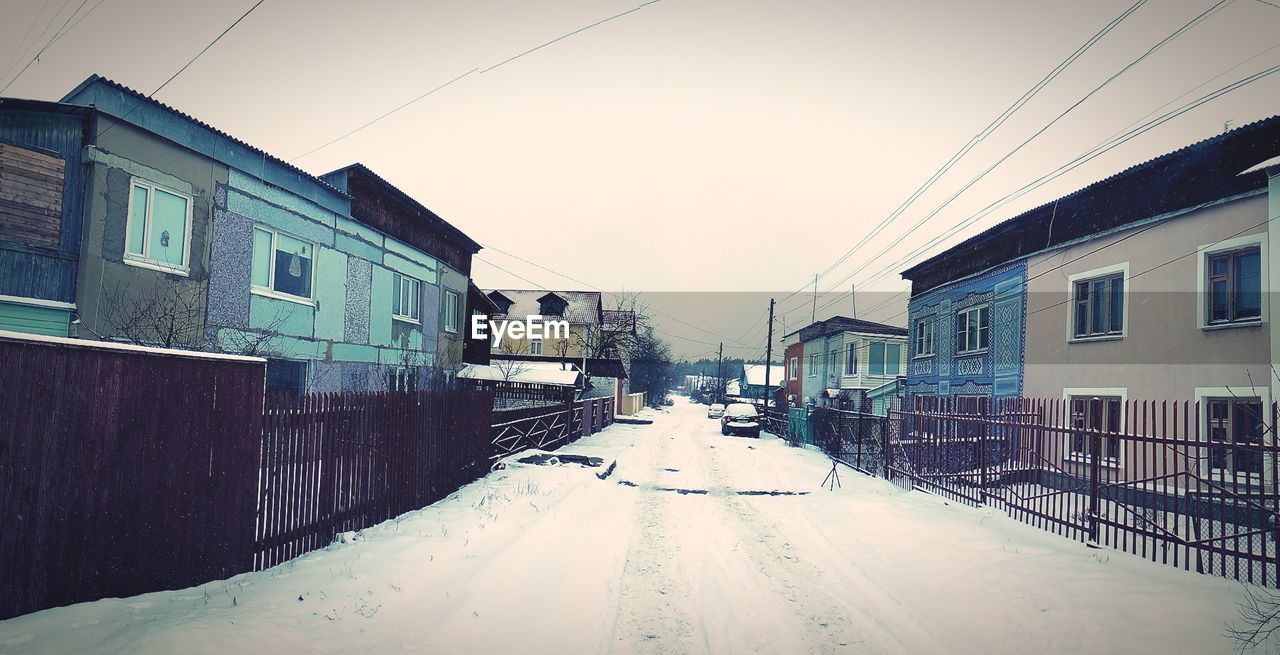 Snowcapped street amidst houses against clear sky