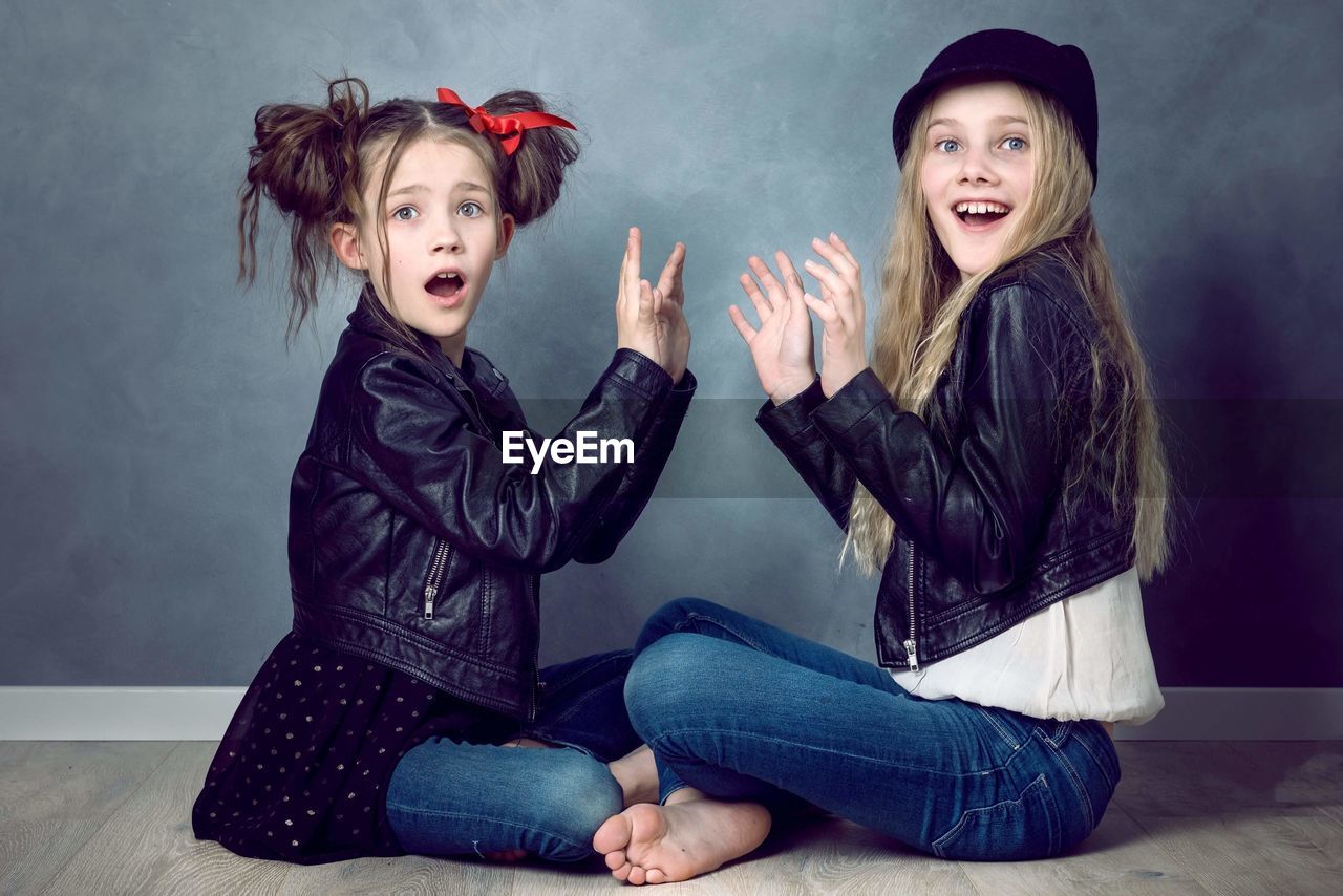 Portrait of girls with mouths open sitting against wall