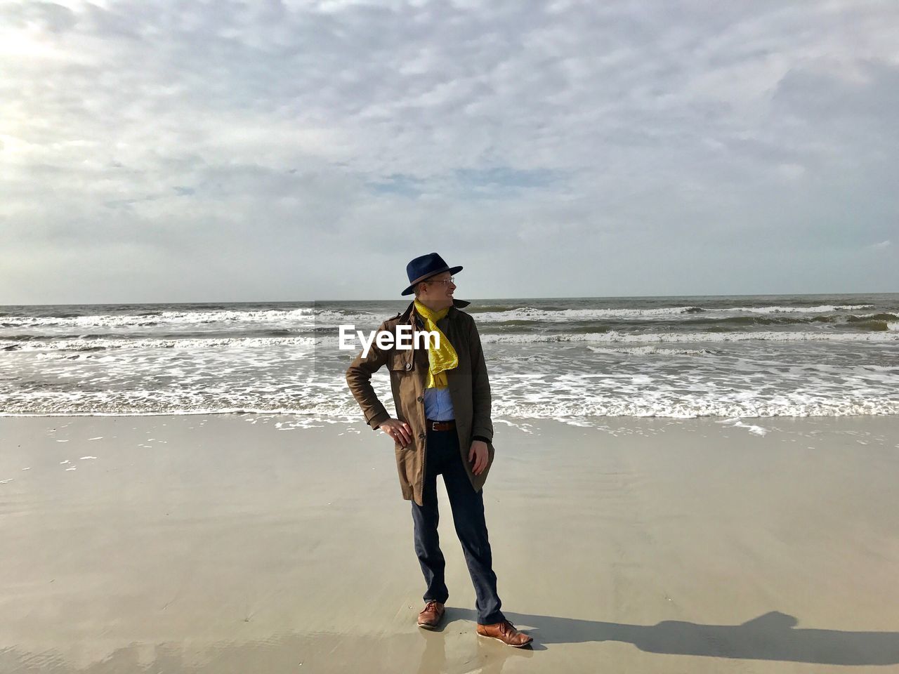 Man standing on shore at beach against cloudy sky