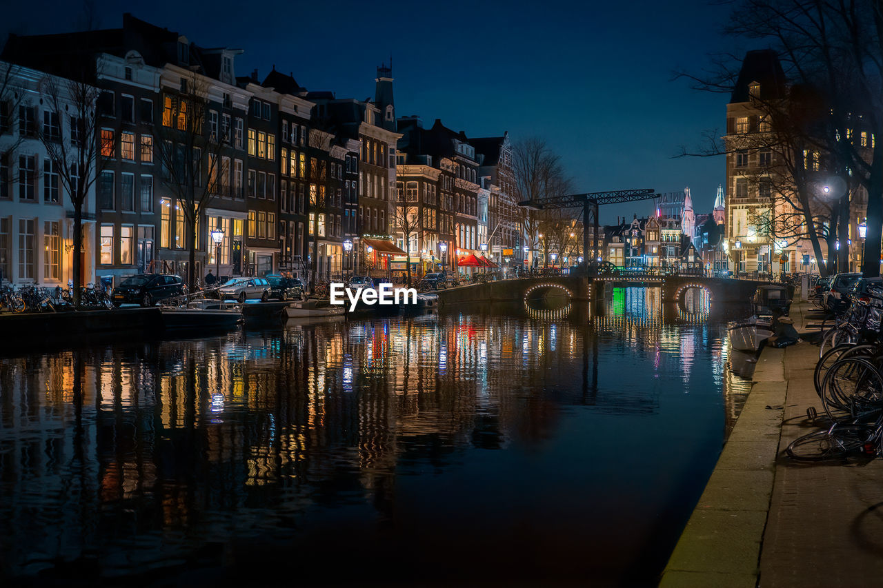 Sailboats moored on illuminated canal by buildings in city at night