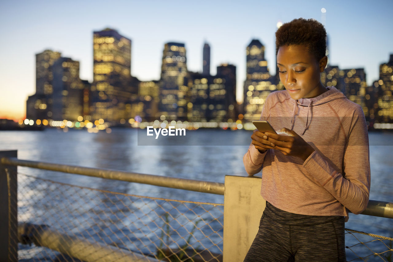 Athlete using mobile phone while standing against illuminated city