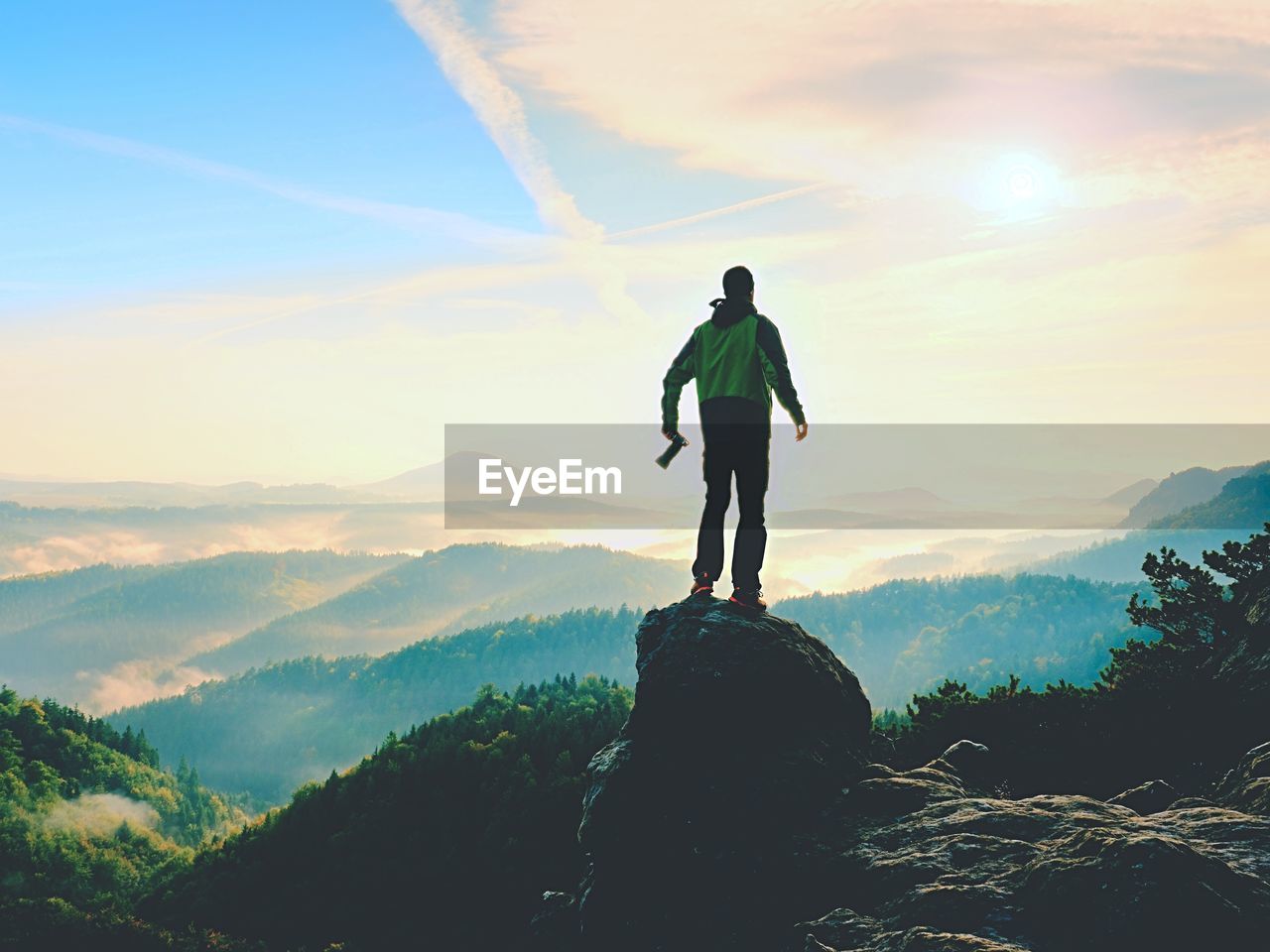 MAN STANDING ON ROCK LOOKING AT MOUNTAINS