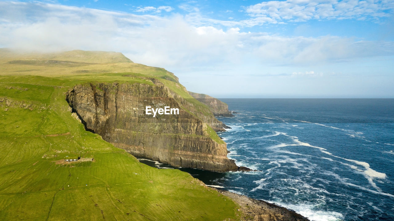 Scenic view of cliff by sea against cloudy sky