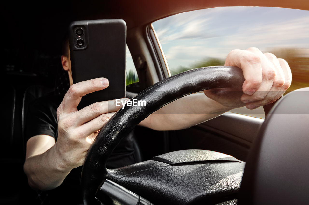 cropped hands of man using mobile phone while driving car