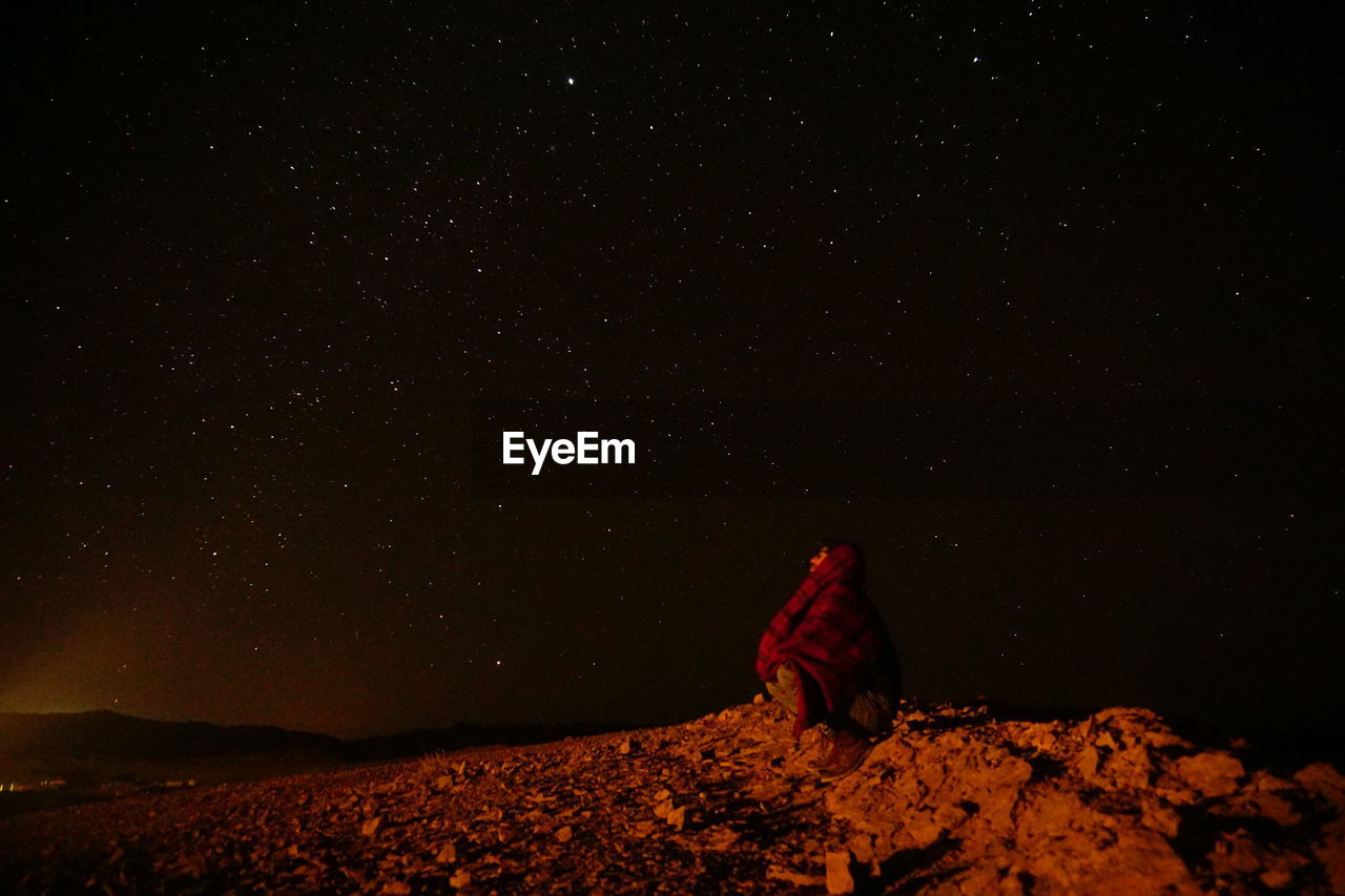 Man with scarf sitting against stars in sky at night