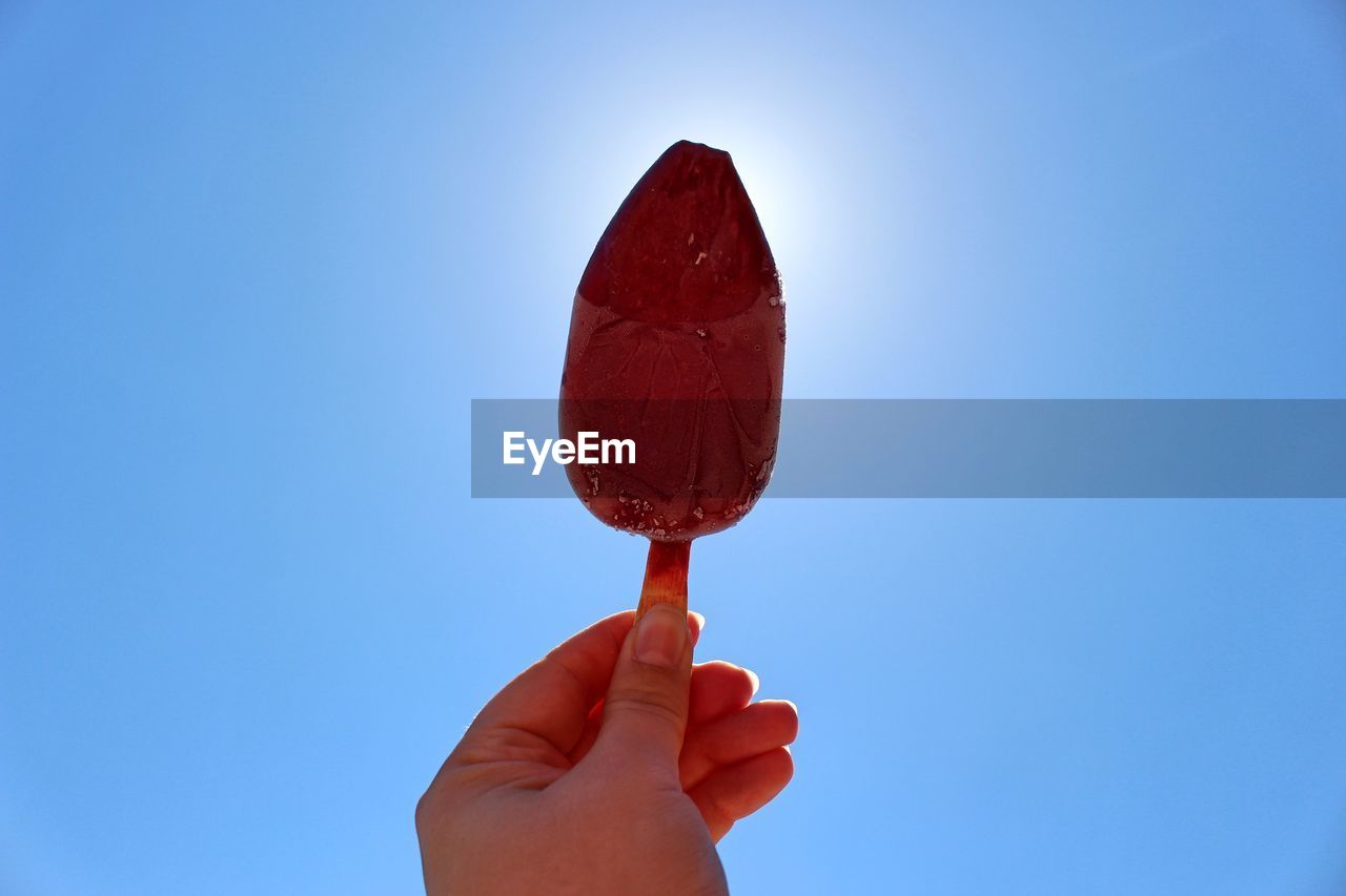 CLOSE-UP OF HAND HOLDING ICE CREAM AGAINST SKY