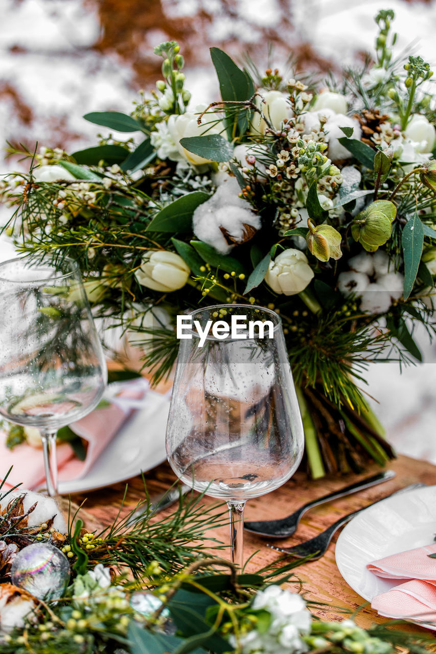 High angle view of wineglasses by flower arrangement on table 