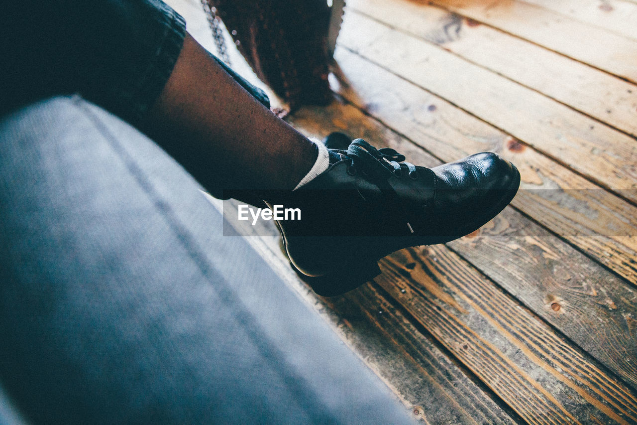 Low section of man wearing black shoes on hardwood floor at home