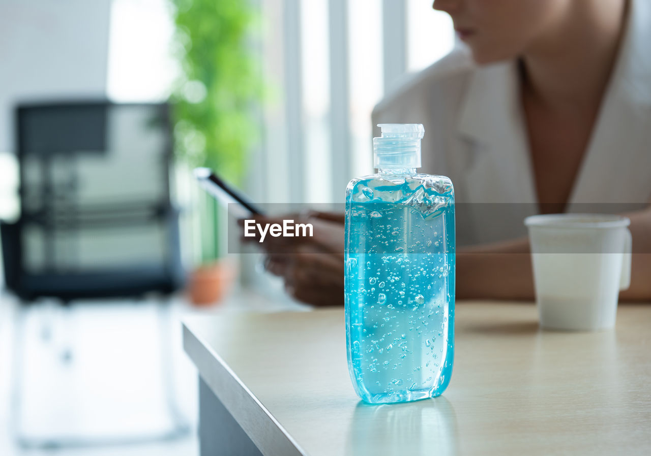 Close-up of woman sitting by bottle on table