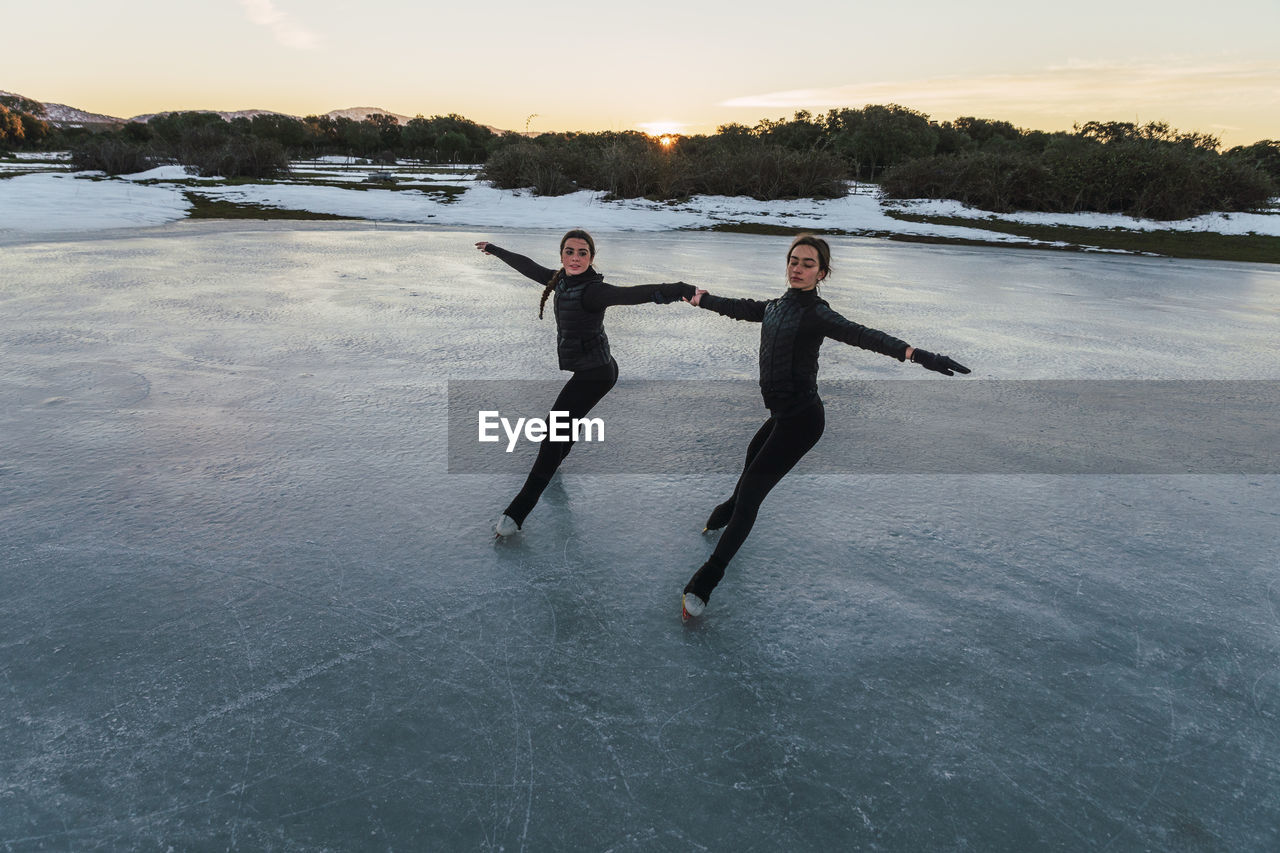 Two female figure skaters practicing together on frozen lake at dusk