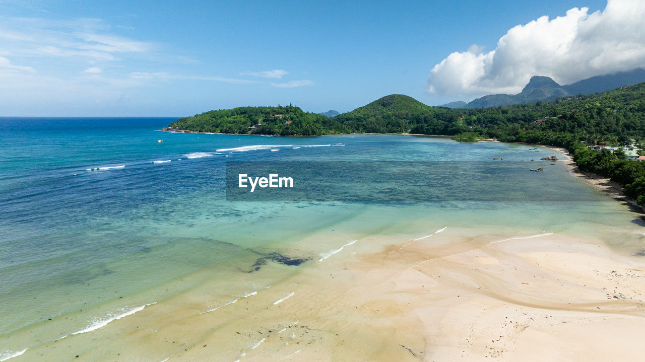 Golden sandy beach, gentle waves, and tropical vegetation. seychelles, mahe.