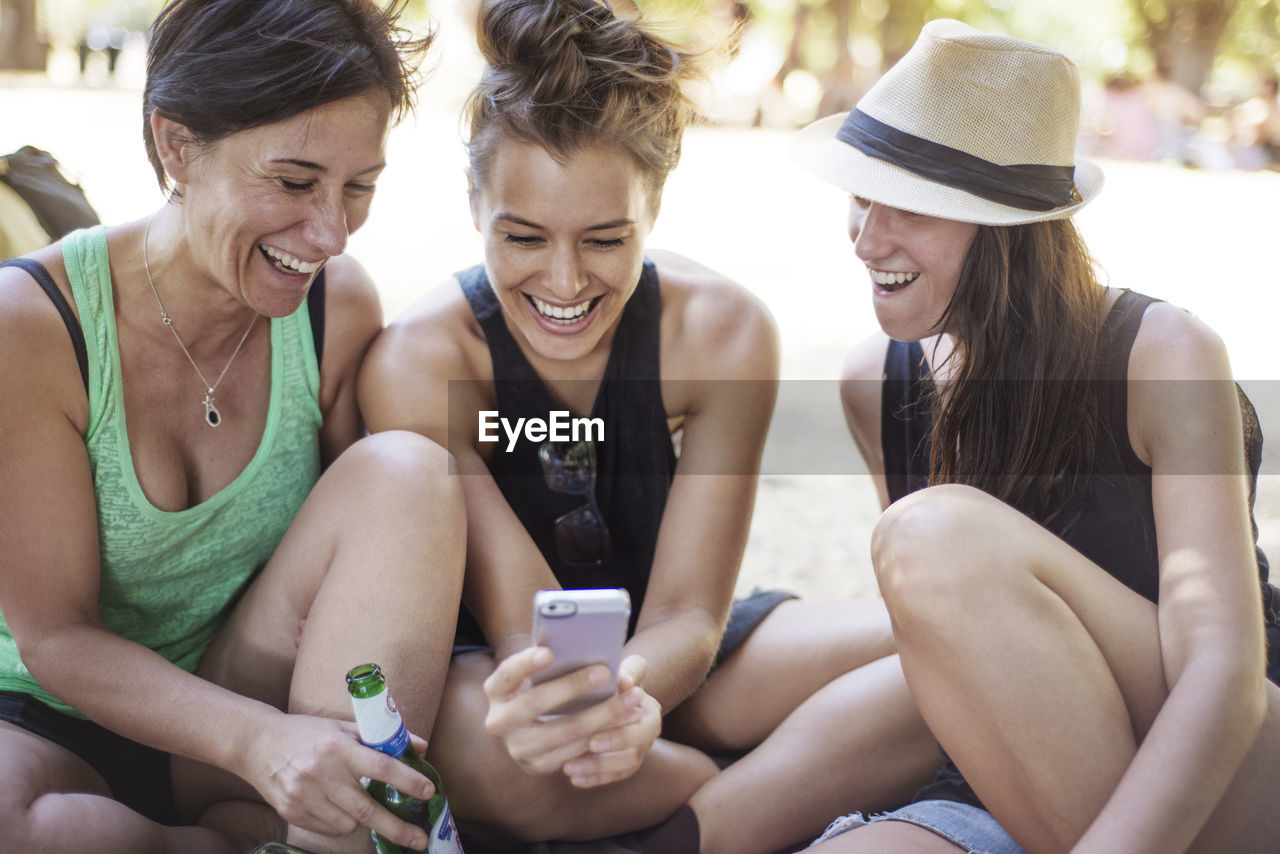 Cheerful female friends looking at phone while enjoying in park