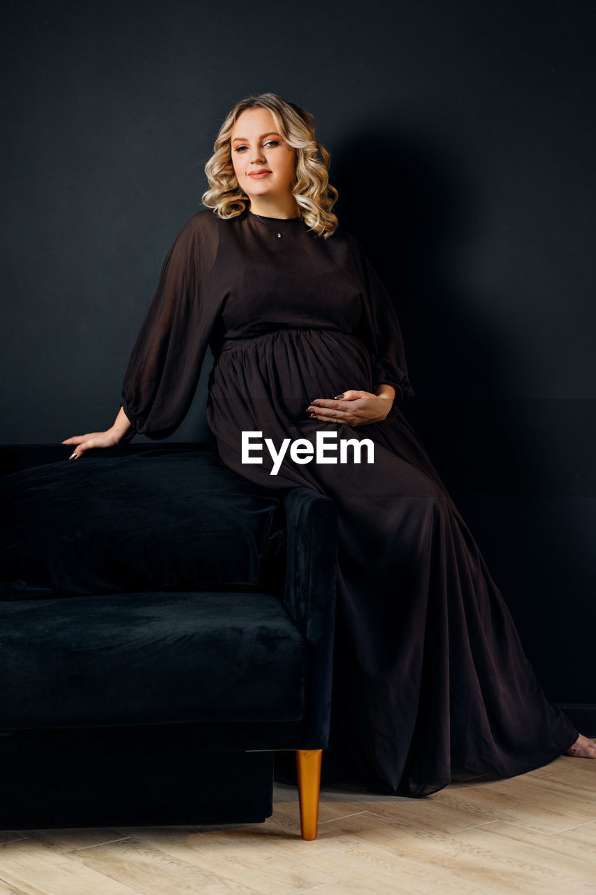 Portrait of pregnant woman sitting on sofa against black background