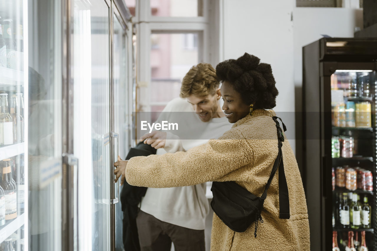 Multiracial couple buying drinks from refrigerated section while shopping at supermarket
