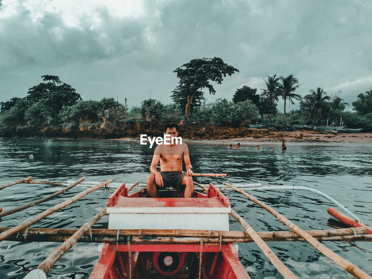 Portrait of shirtless man sitting on boat in river against sky