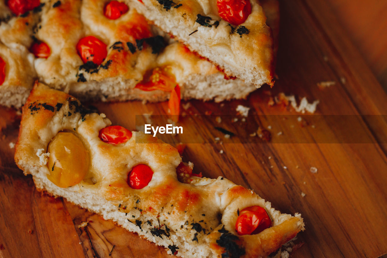 Homemade italian focaccia slices, with tomato and olive oil on a rustic wooden background.