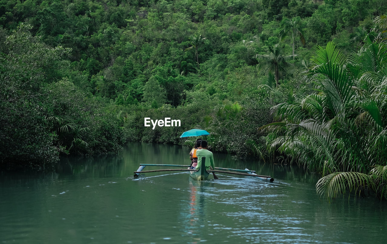 Rear view of people in boat on lake against trees