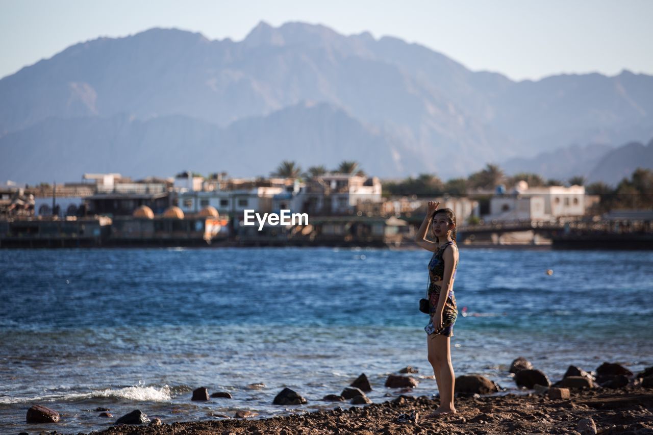 MAN IN SEA BY CITY AGAINST MOUNTAINS