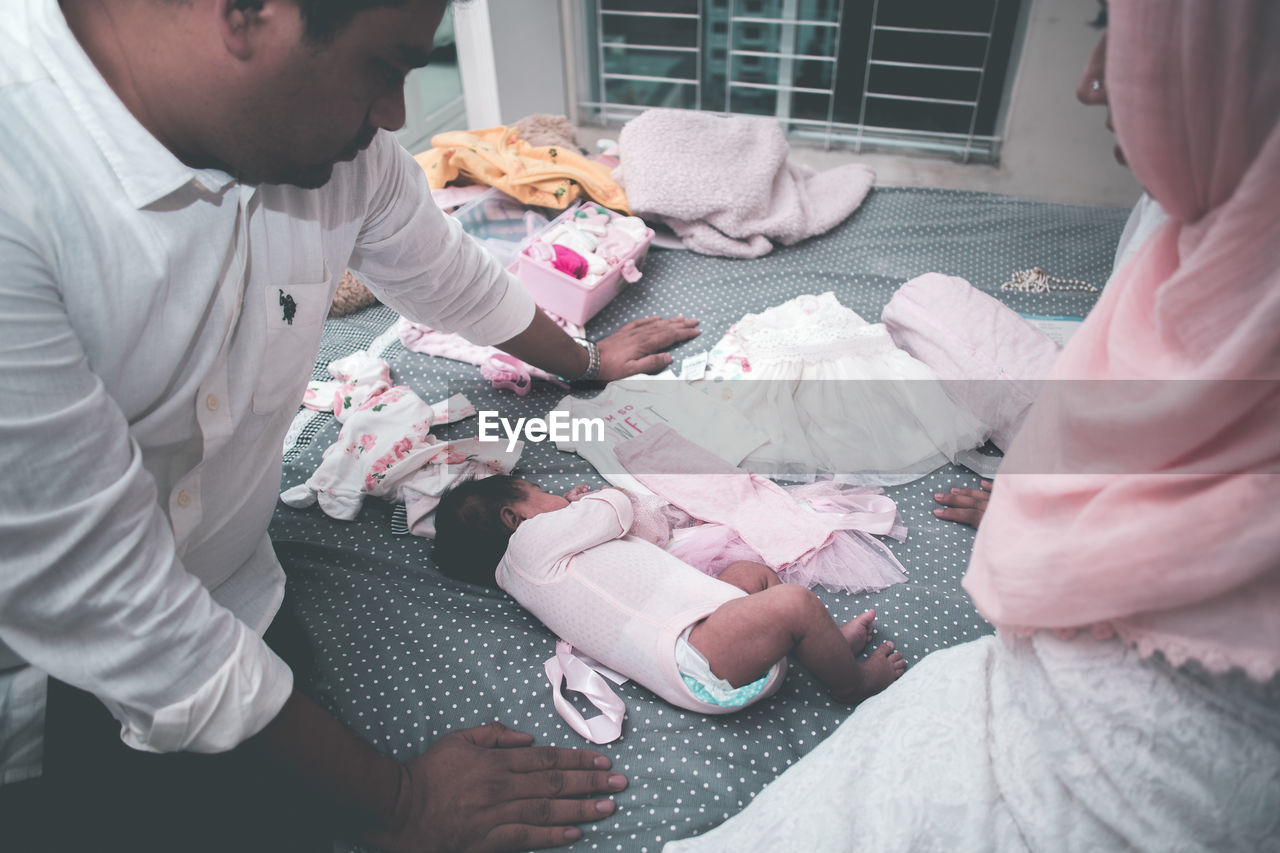 High angle view of parents looking at baby girl sleeping on bed at home