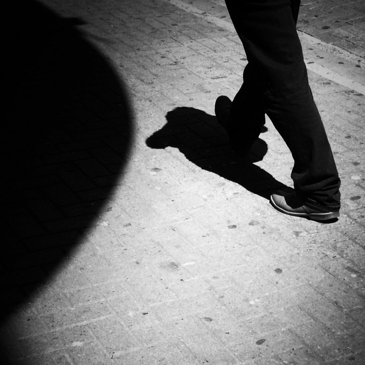 Low section of man walking on footpath during sunny day