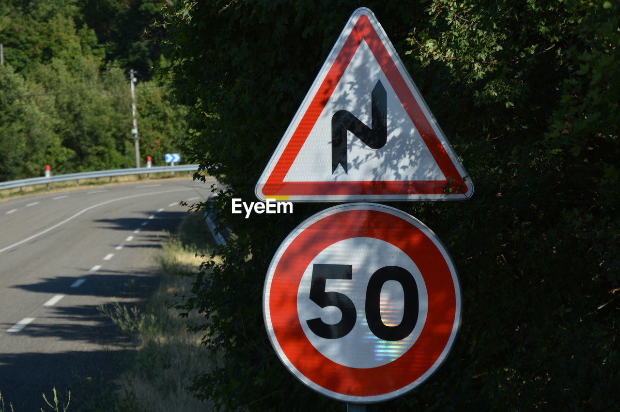 sign, road, traffic sign, road sign, communication, transportation, lane, warning sign, plant, symbol, signage, guidance, shape, no people, geometric shape, tree, triangle shape, nature, day, outdoors, red, information sign, road marking, city, circle, mode of transportation, speed limit sign, street, marking