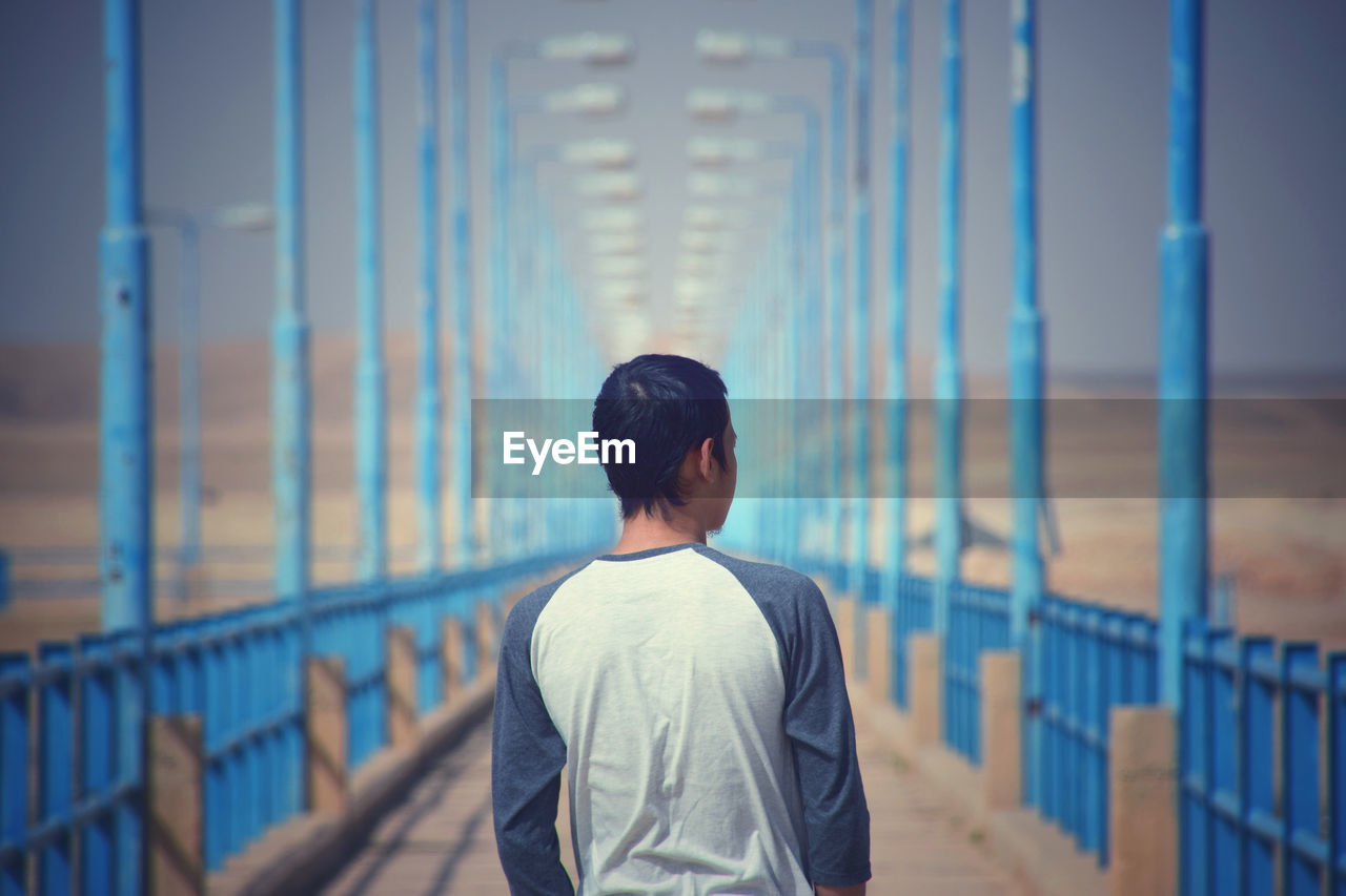 Rear view of man standing by railing against bridge