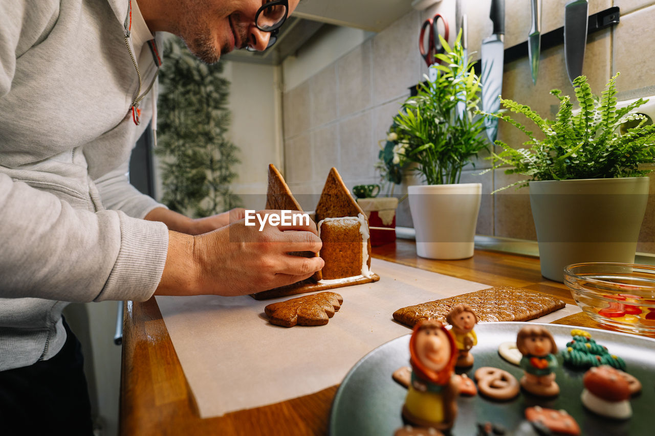 Midsection of man preparing gingerbread house on kitchen counter