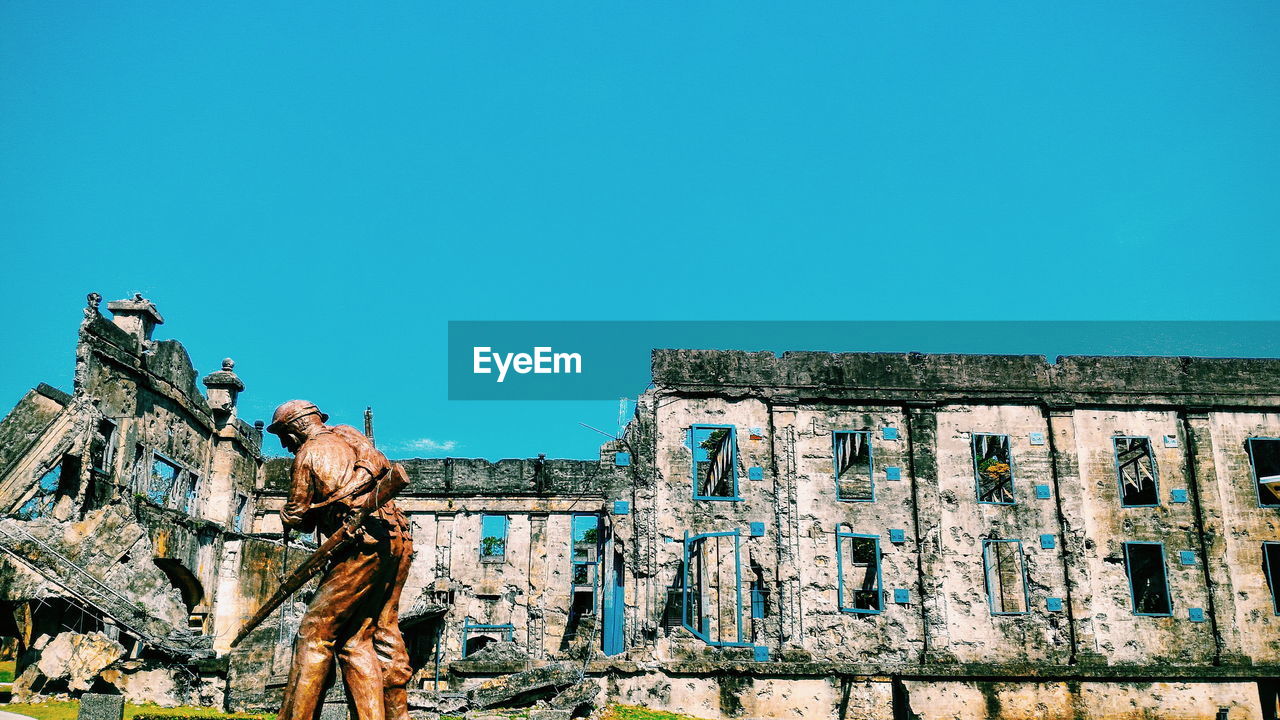 Soldier statue by old ruin historic building against clear blue sky
