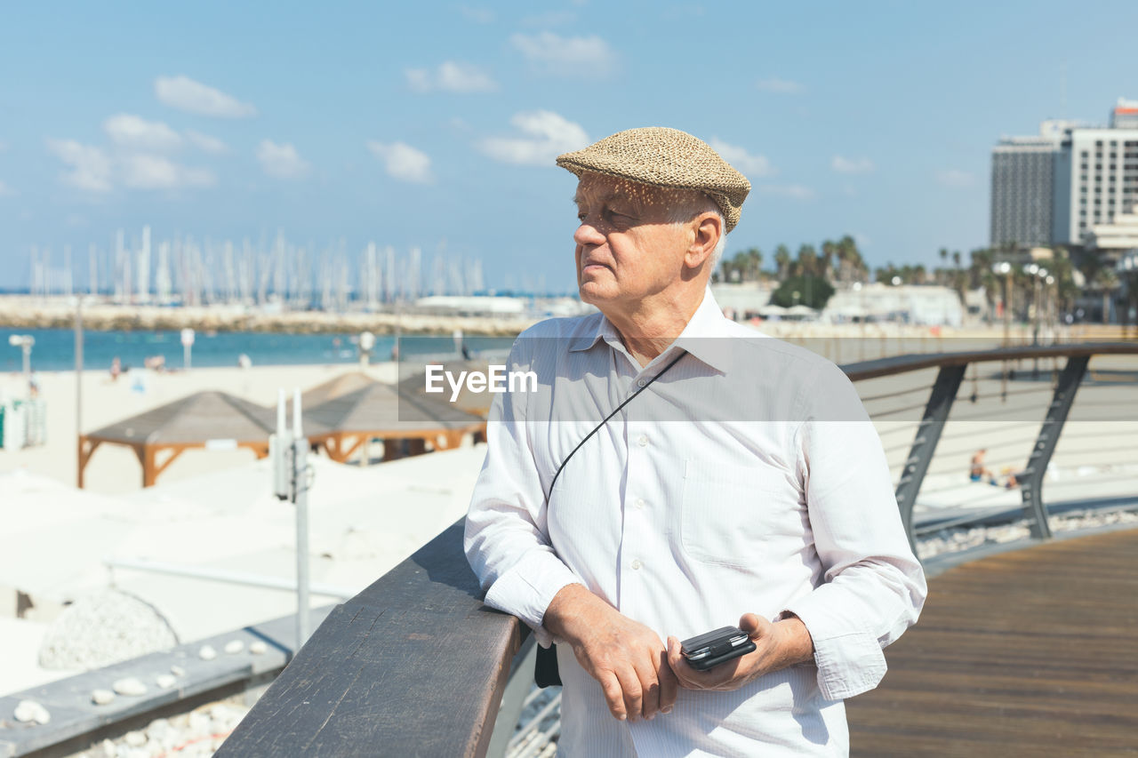 Senior man looking away while standing by railing on promenade