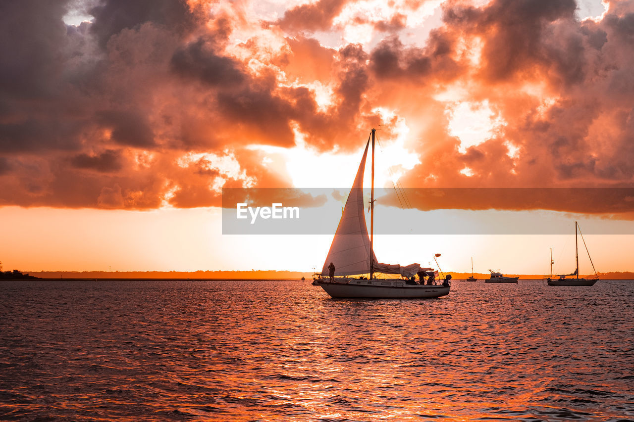 SAILBOAT SAILING IN SEA AGAINST SKY DURING SUNSET