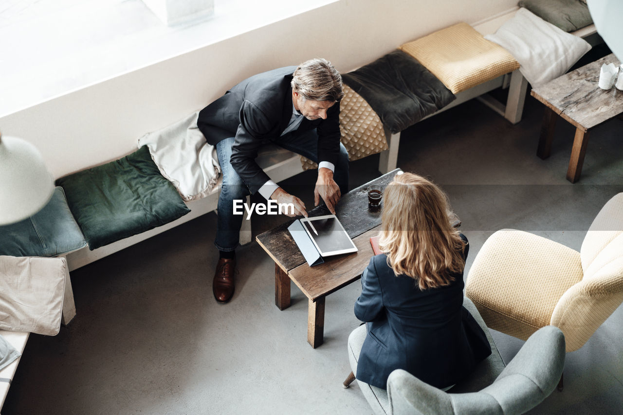 Mature businessman discussing over digital tablet with female colleague in cafe