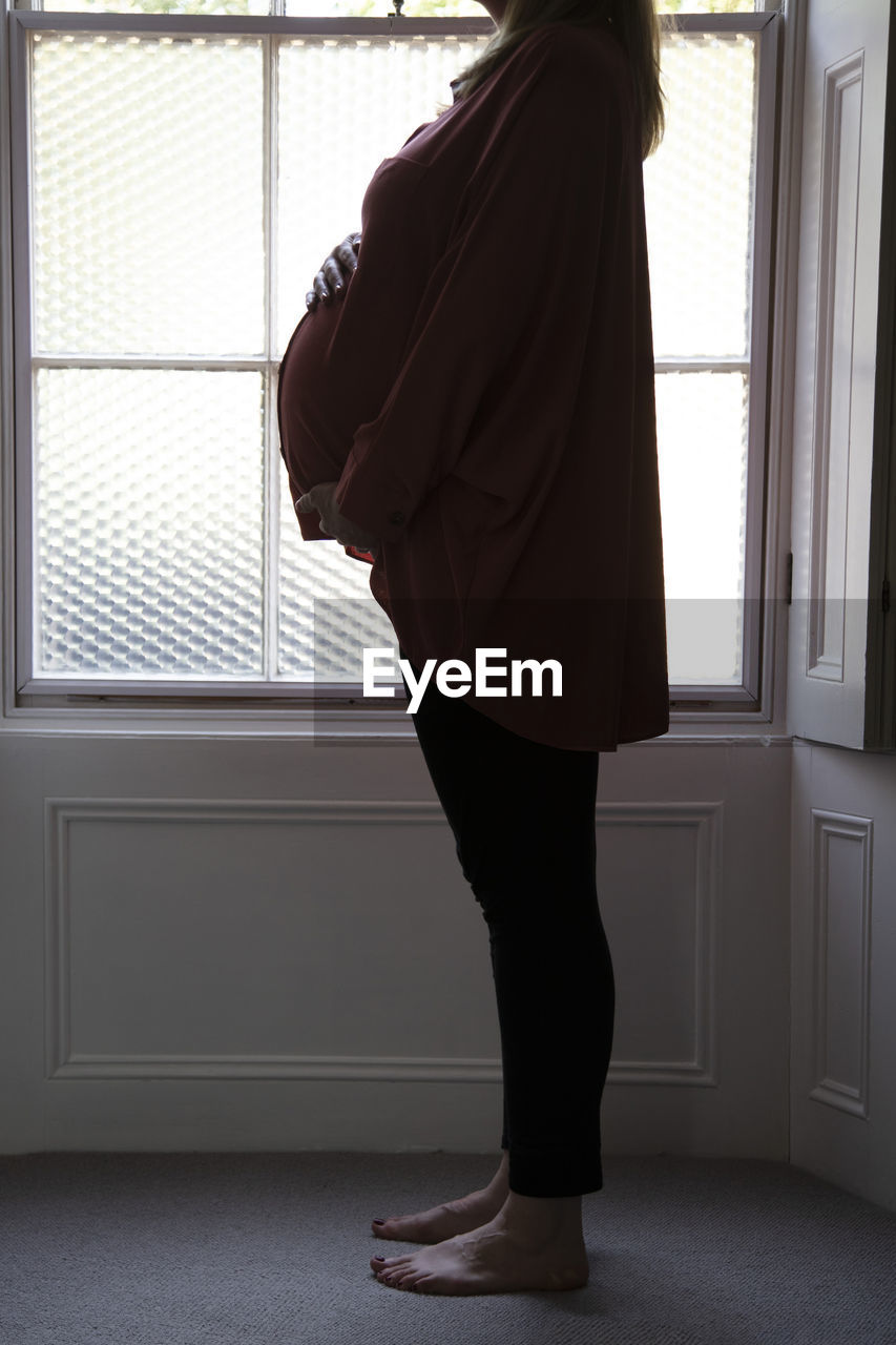 Side view of pregnant woman standing by window at home