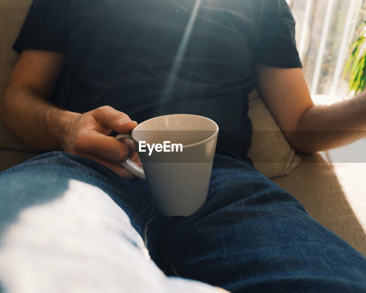 Midsection of man having coffee while sitting on sofa at home