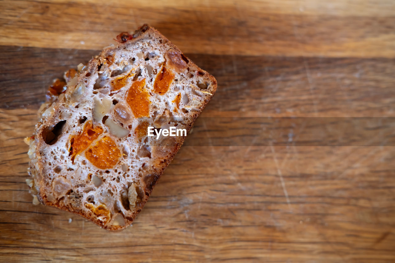 Piece of whole grain bread with candied fruits on a wooden background, copy space