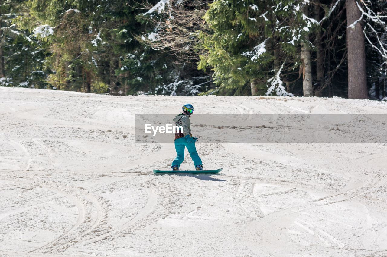 Full length of woman snowboarding against trees