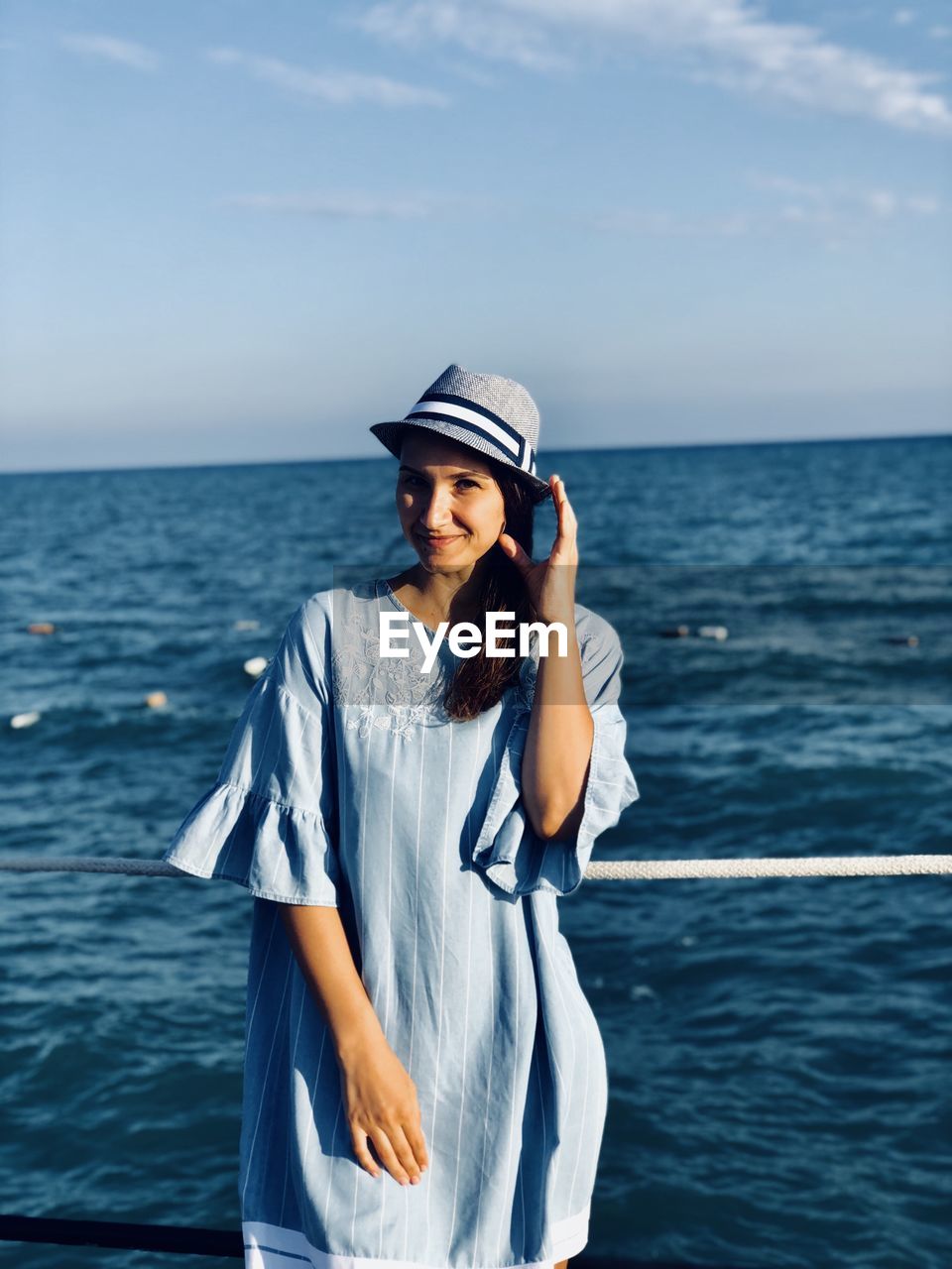 Portrait of woman wearing hat standing against sea