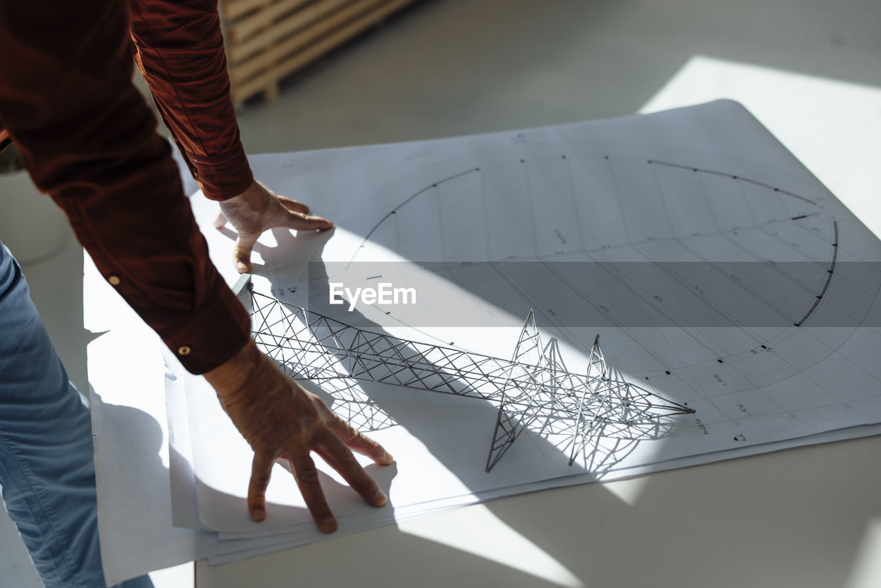 Hands of businessman by electric pylon model on blueprint at desk