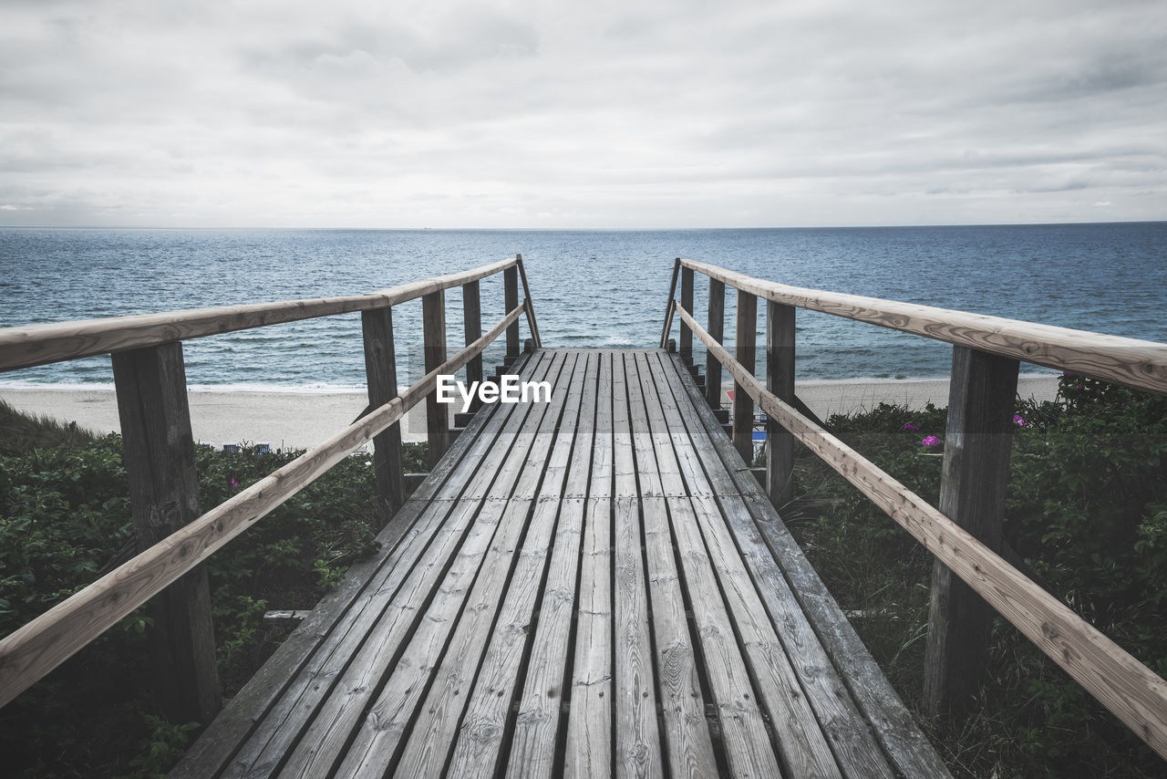 Wooden bridge over roses bushes towards beach and north sea water, on sylt island, germany.