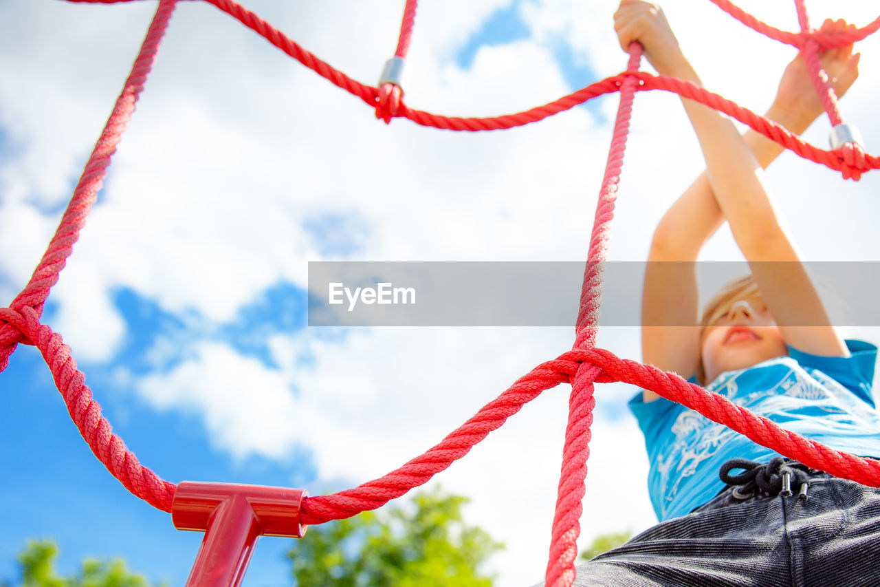 Low angle view of boy climbing rope against sky