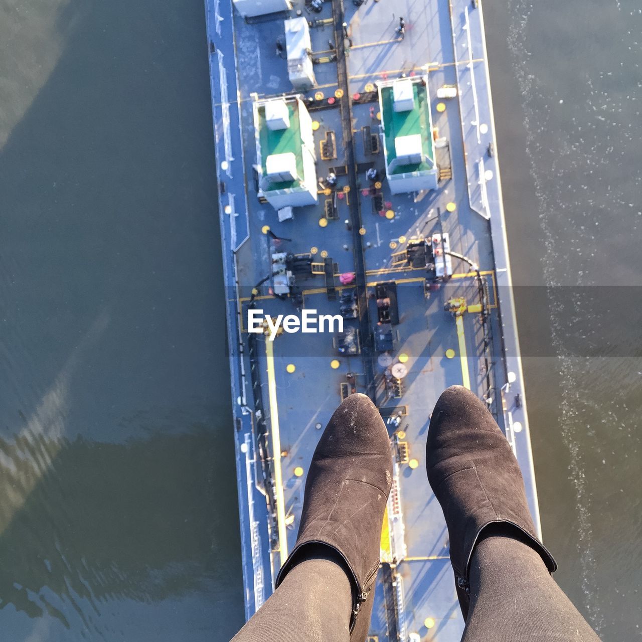 Low section of female wearing suede boots against cargo ship