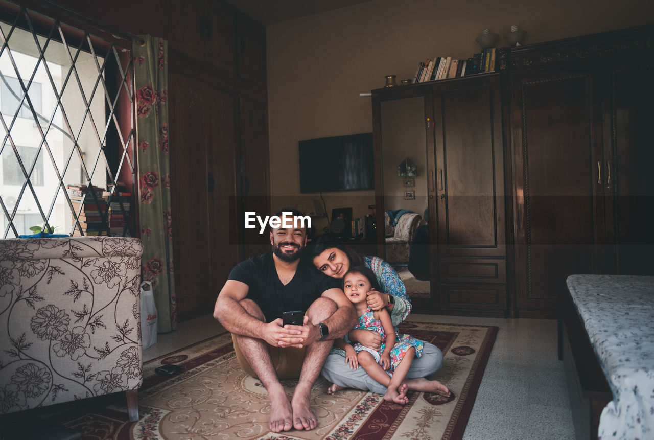 Portrait of smiling parents sitting with daughter on carpet in living room at home