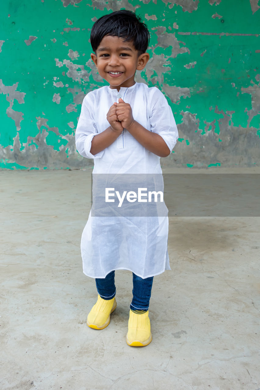 PORTRAIT OF CUTE SMILING BOY STANDING AGAINST WALL