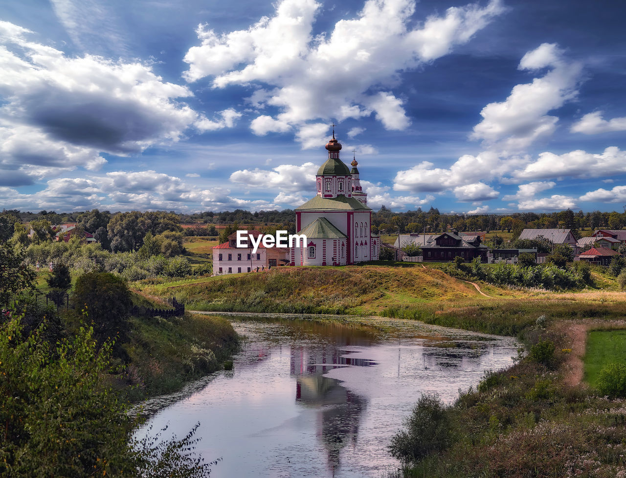 Romantic cloudy sky over summer suzdal city with residential houses, orthodox church and river