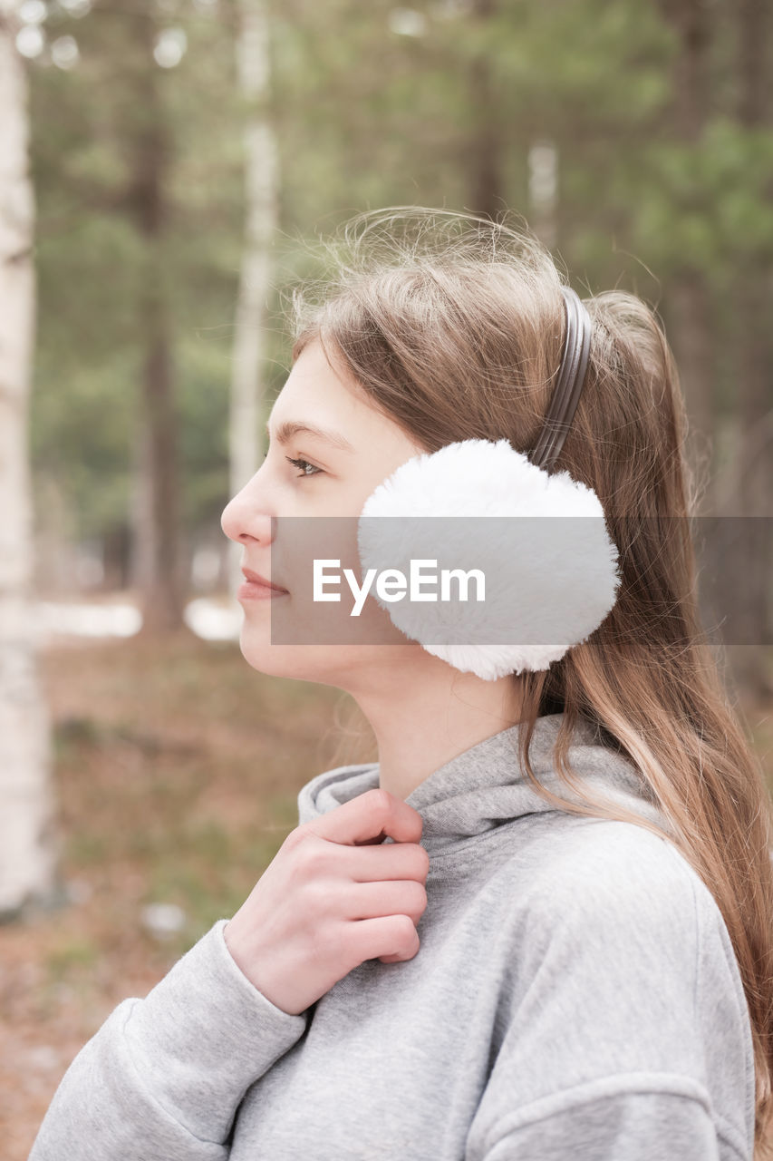 Outdoor portrait of teenager girl wearing white earmuffs. close up of a girl walking in the forest. 